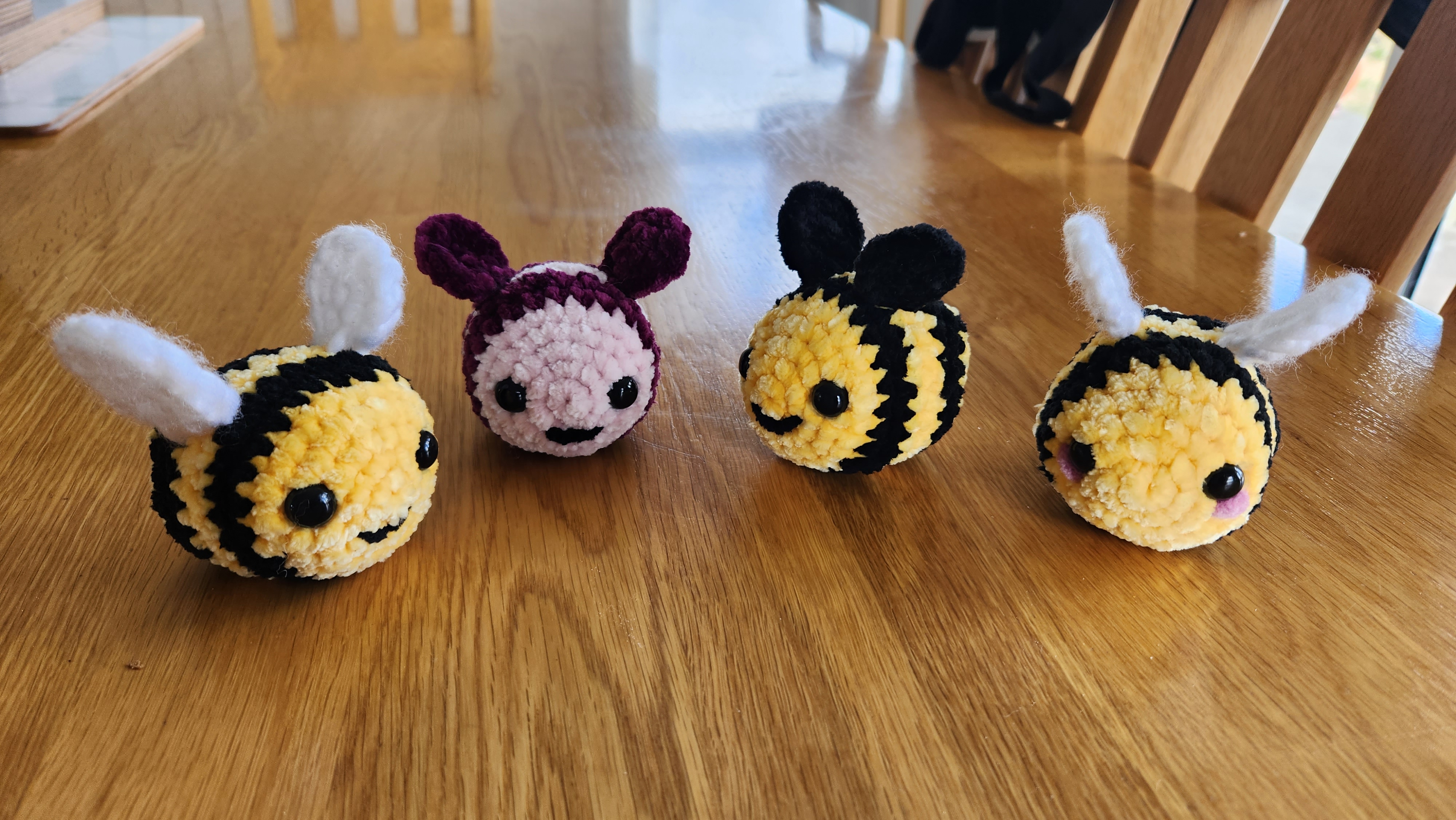 Four small crocheted bumblebees in yellow, black and pink