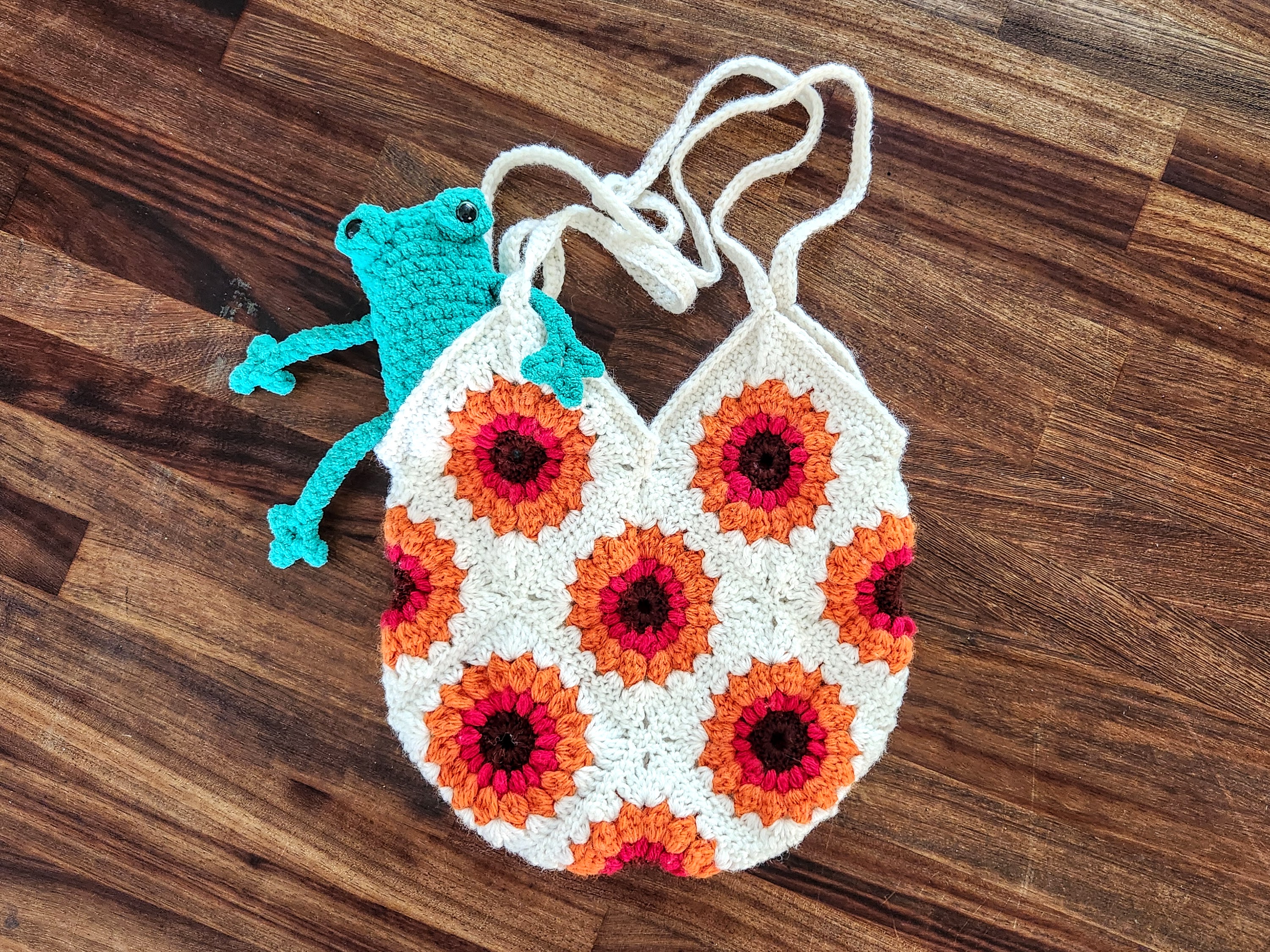 A cream, orange and berry granny-square tote bag with a sunflower motif and a small teal frog