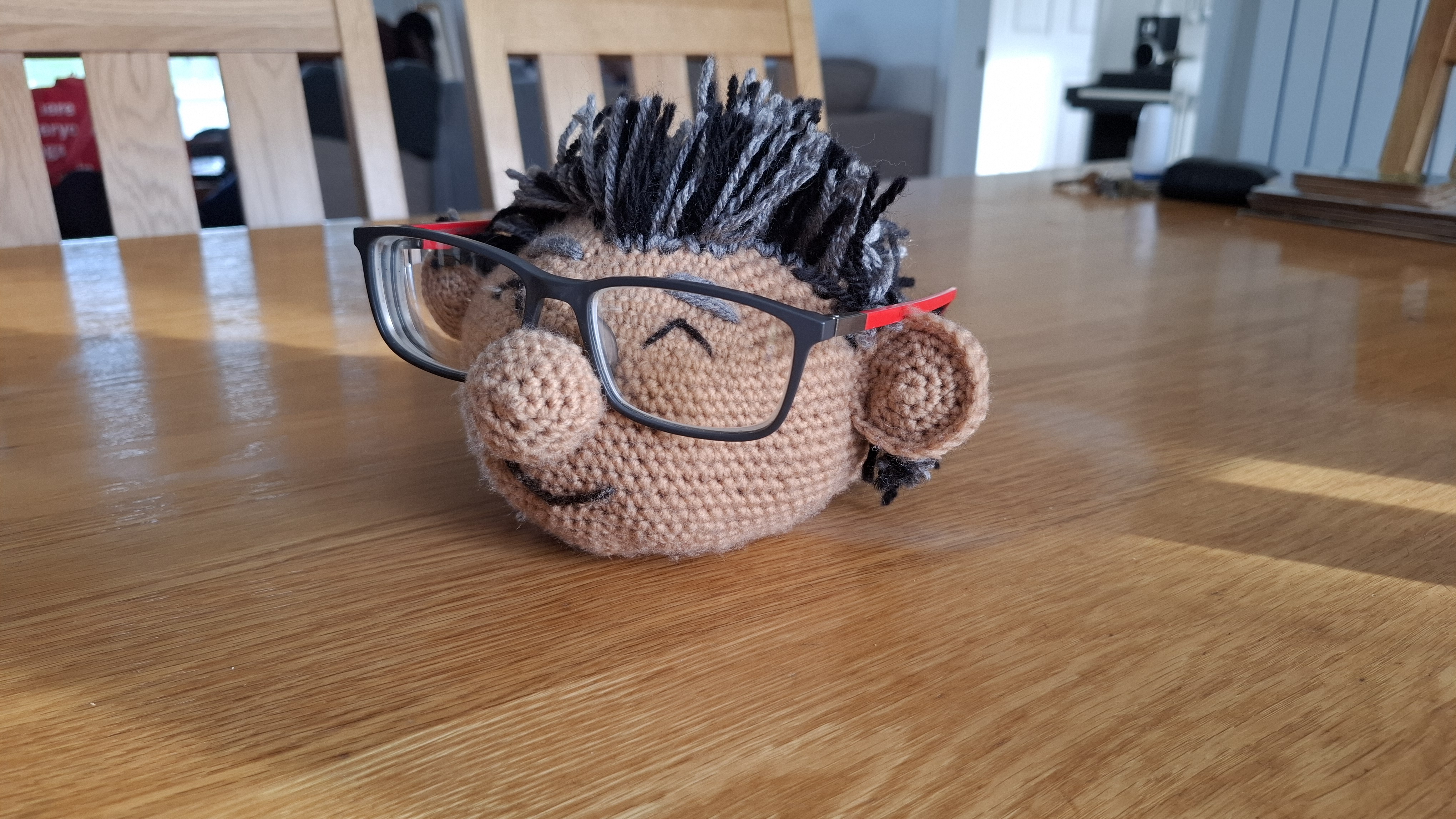 A crocheted character head that holds a pair of glasses on its nose