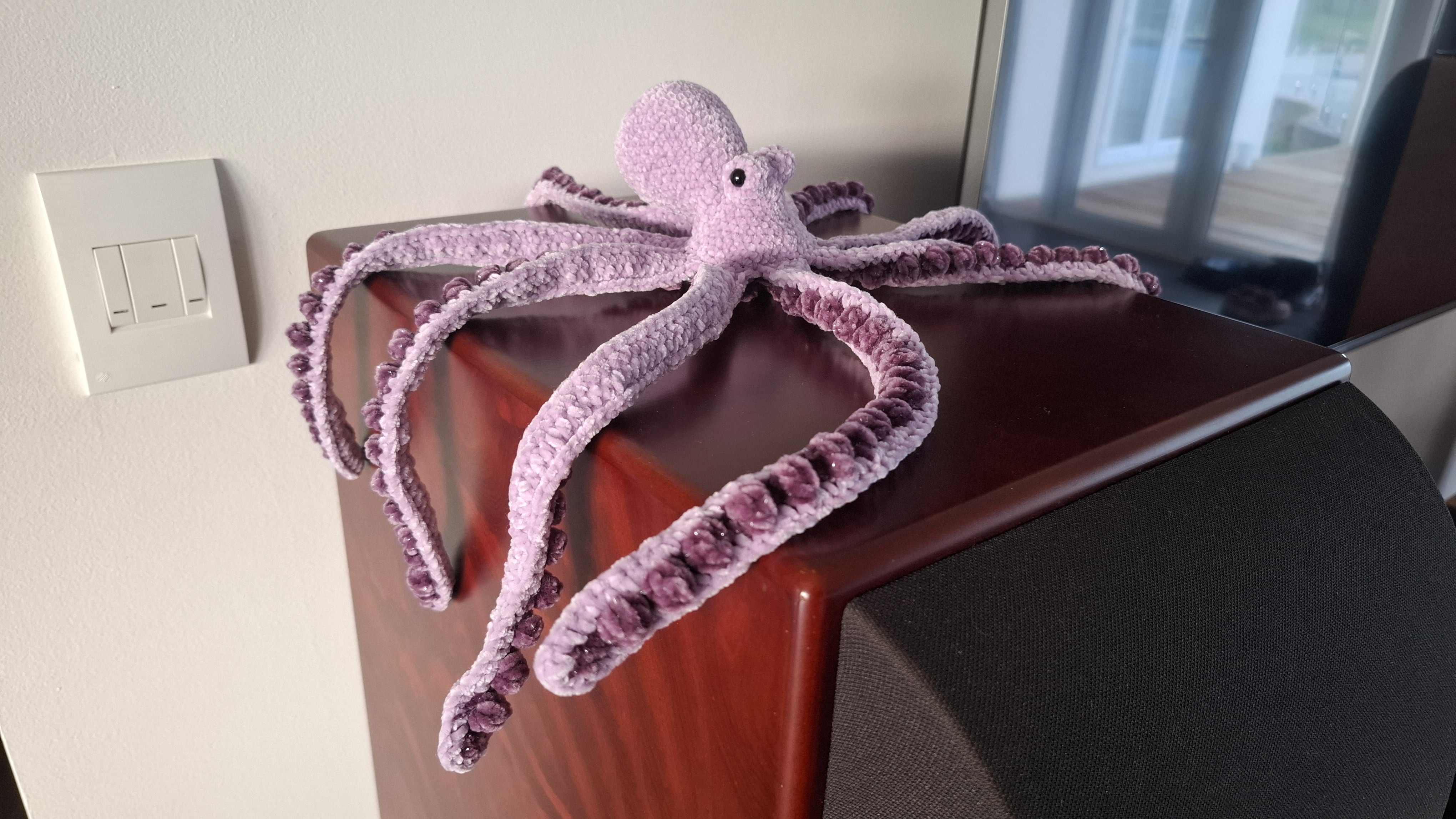 A large purple chenille crocheted octopus with curling tentacles