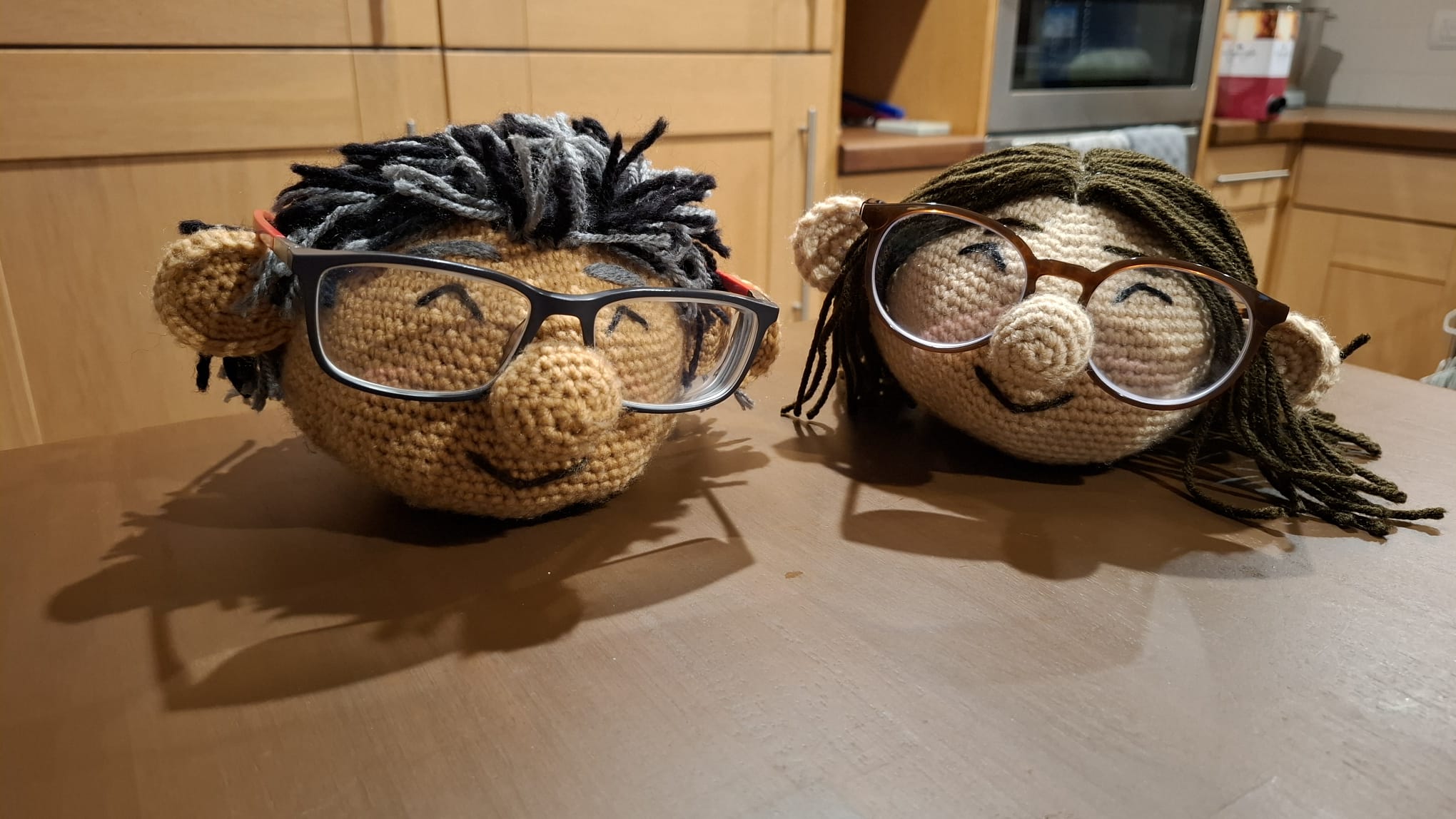 Two crocheted character heads holding real glasses