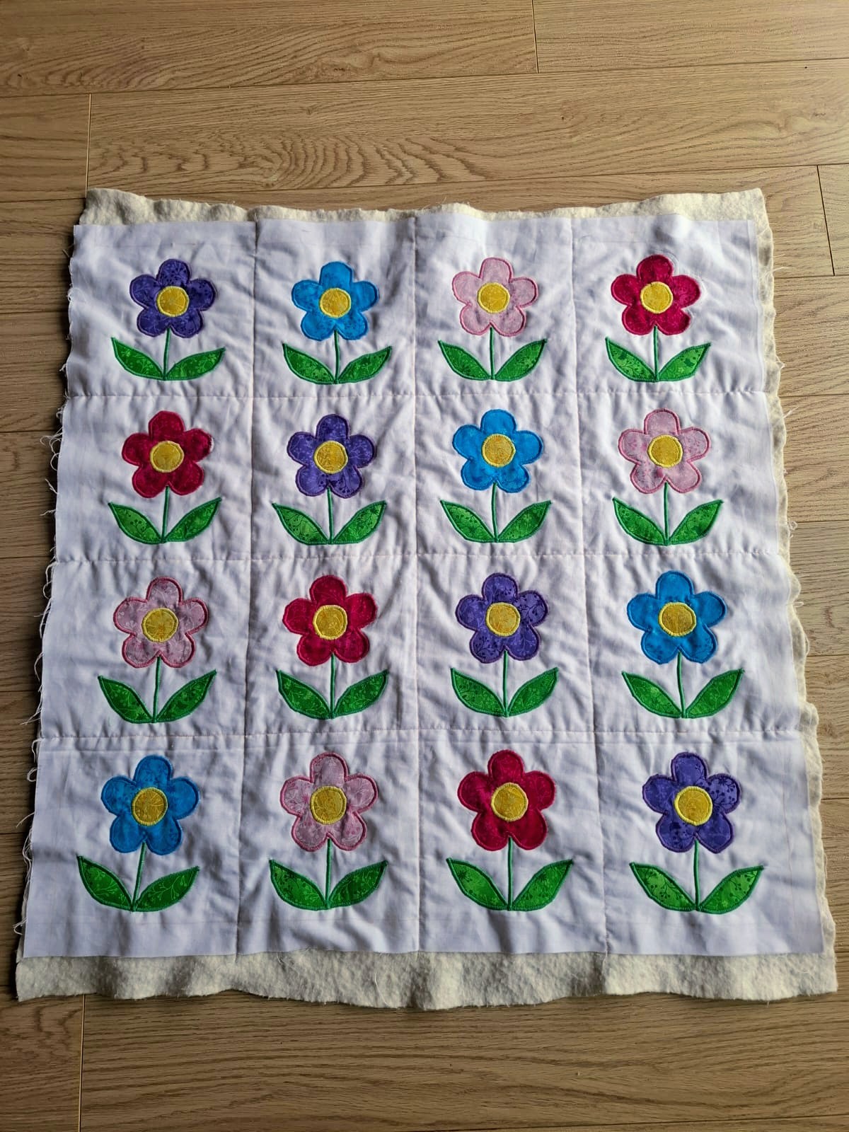 A white quilted blanket with colourful appliqué flowers, made for a neonatal unit