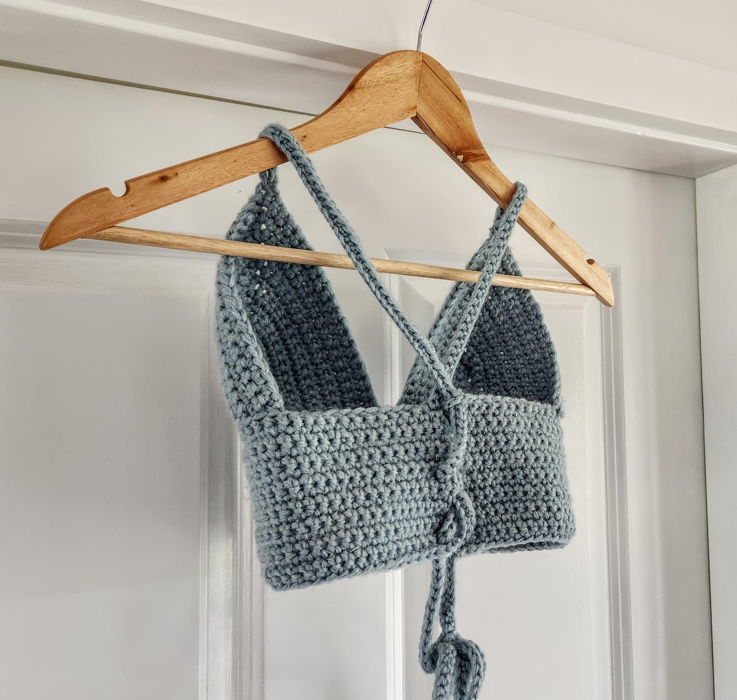 Back view of a sage-green crocheted halter top on a wooden hanger