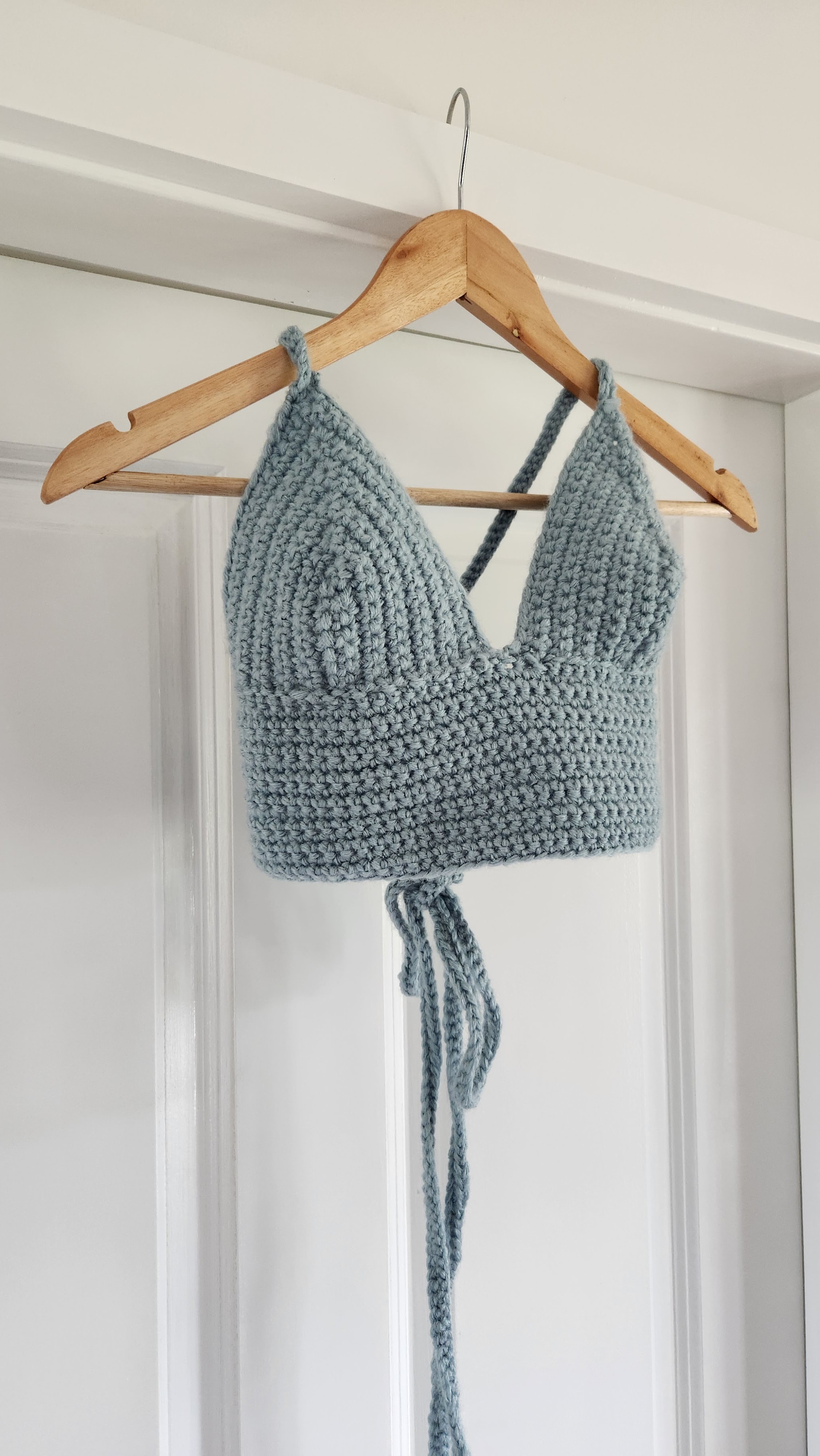 A pale blue crocheted halter top on a hanger