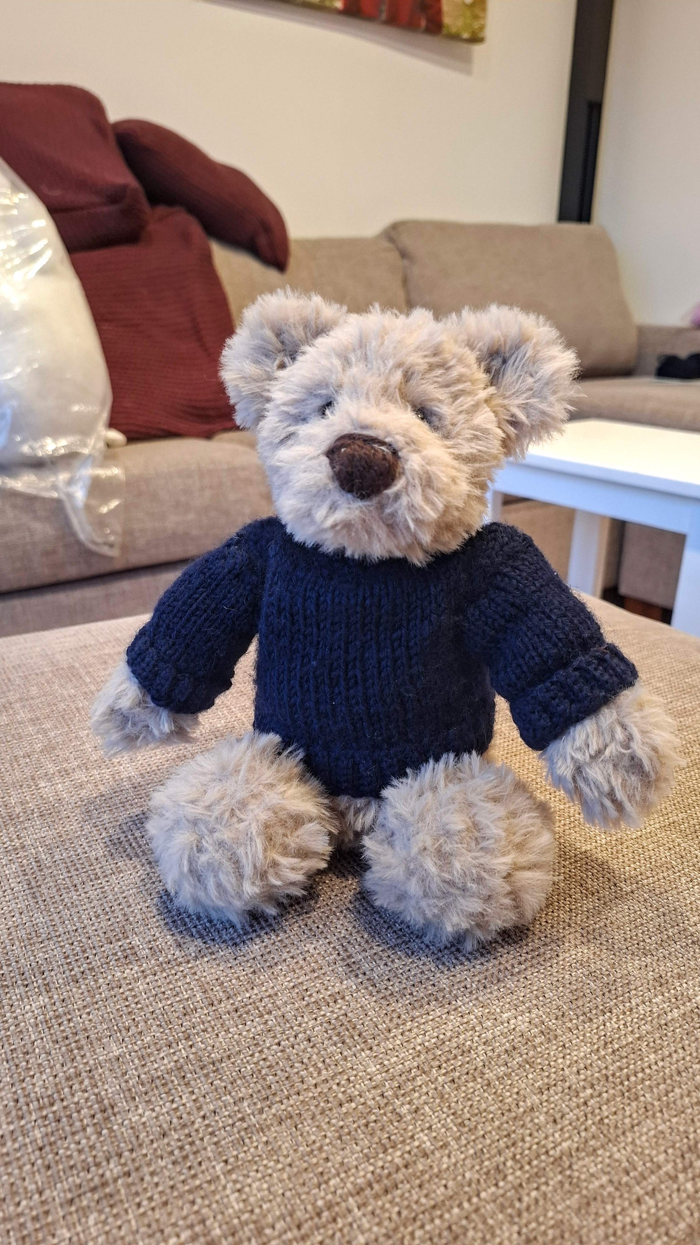 A fluffy light-brown crocheted teddy bear wearing a hand-knitted navy Guernsey jumper