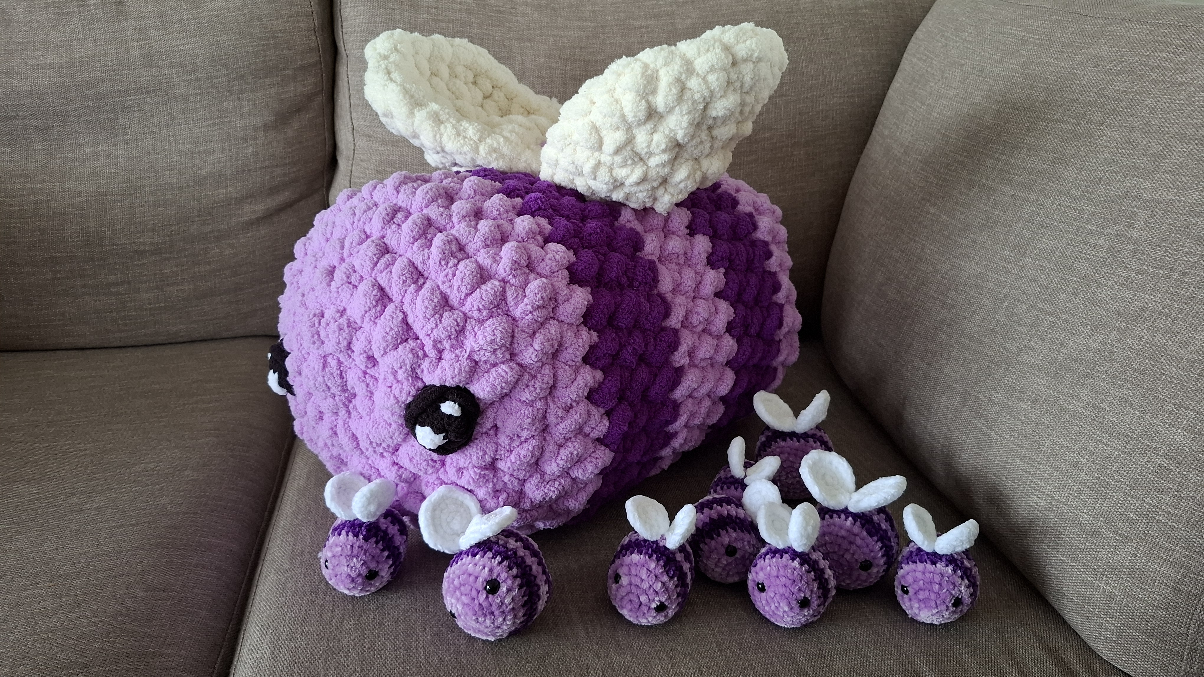 A giant crocheted purple bee surrounded by a colony of small purple bees on a table