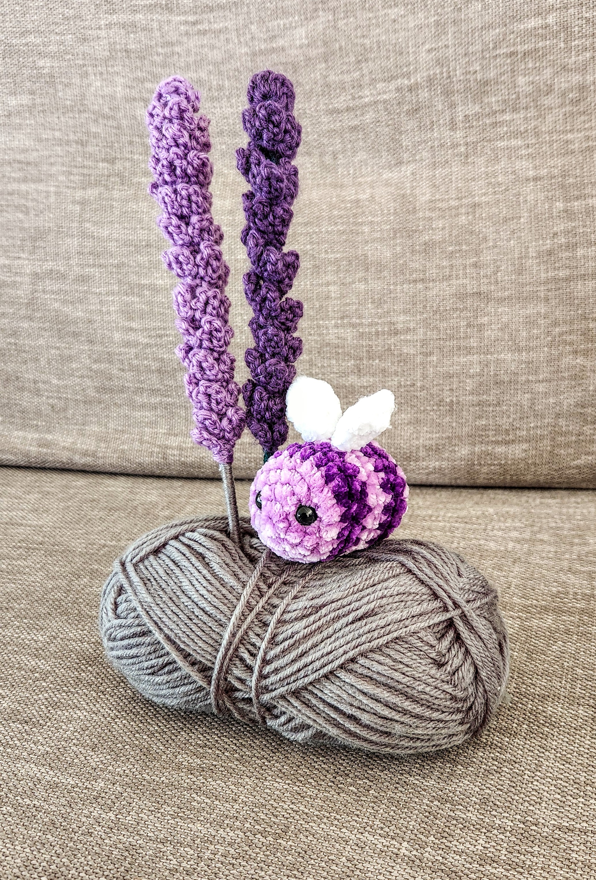 A purple crocheted bee with crocheted lavender stems resting on a ball of wool