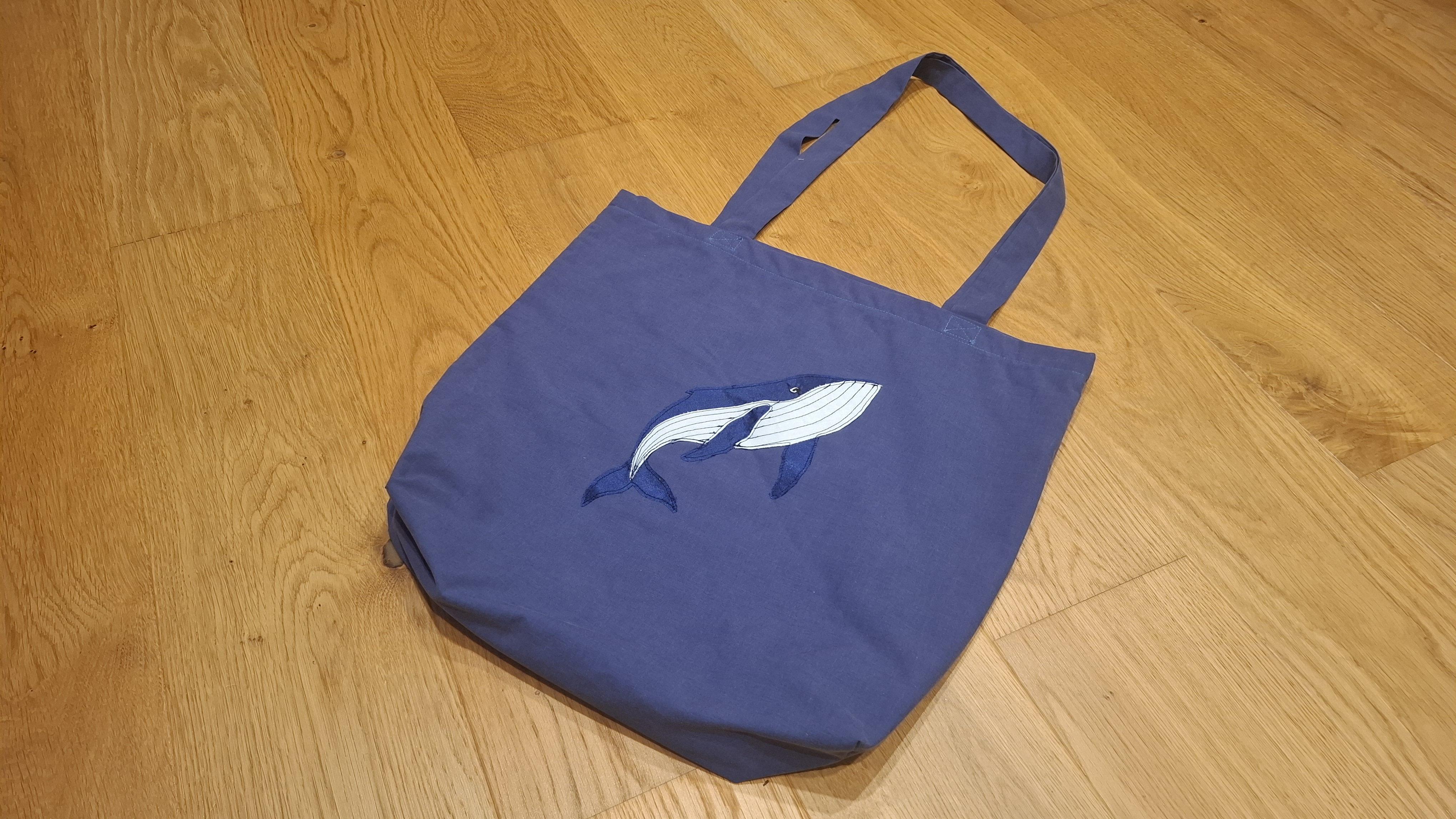 A navy tote bag with an appliqué humpback whale